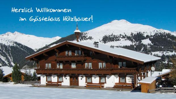 a large wooden building with a snow covered mountain at Apartment Hölzlbauer in Krimml