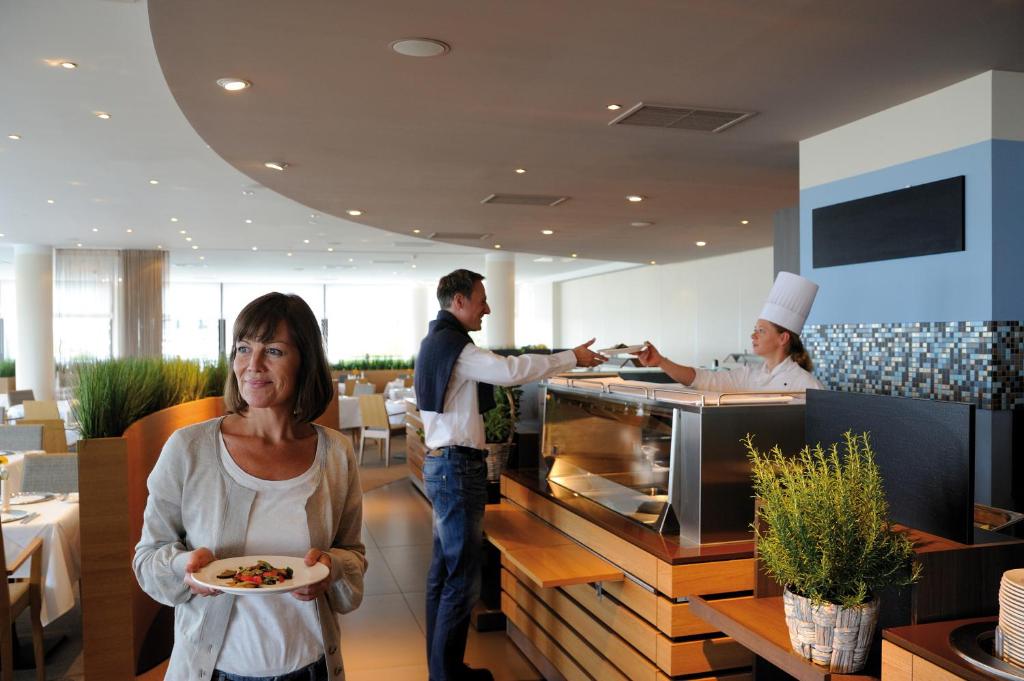 a woman holding a plate of food in a restaurant at Hotel Neptun in Warnemünde