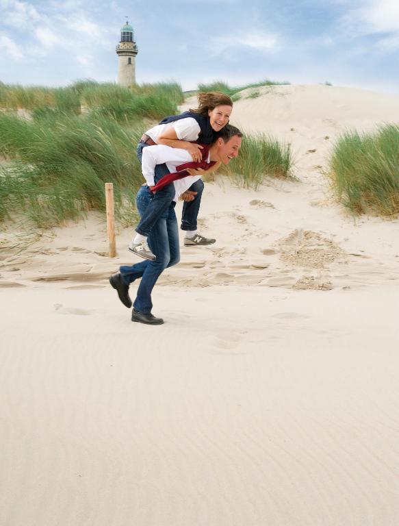 a man carrying a woman on a beach with a lighthouse at Hotel Neptun in Warnemünde