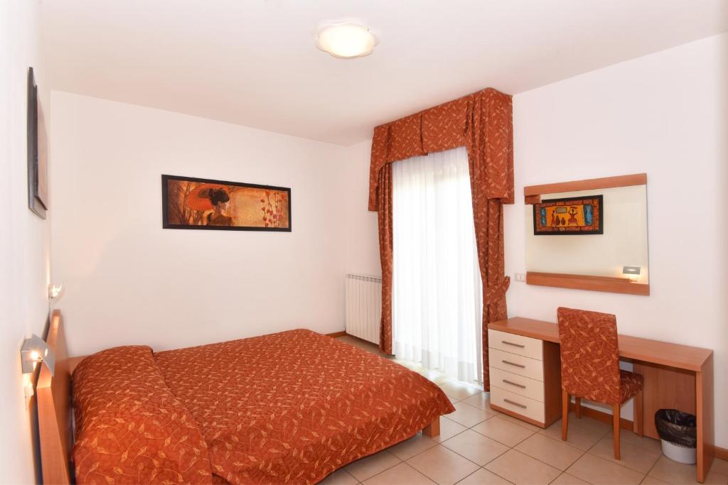 a bedroom with a bed and a desk and a window at Hotel Villa Olga in Caorle