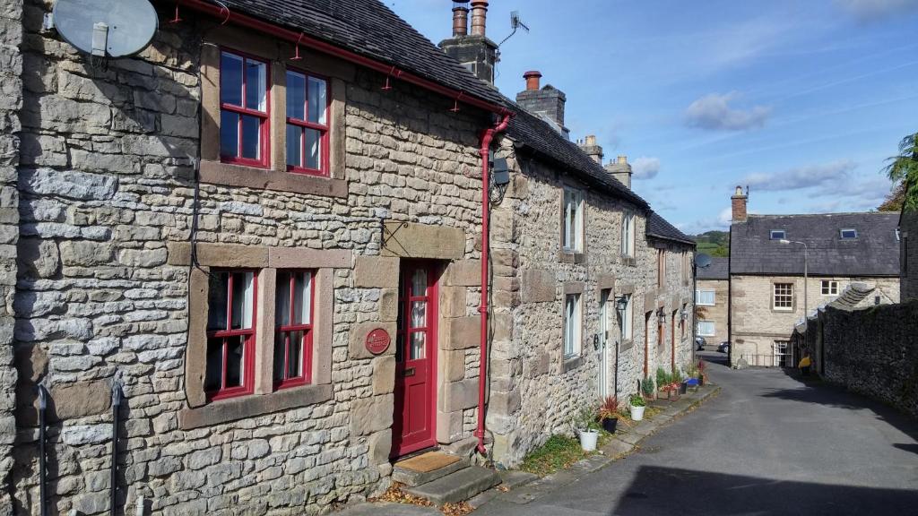 an old stone building with red doors and a street at Clover Cottage in Winster