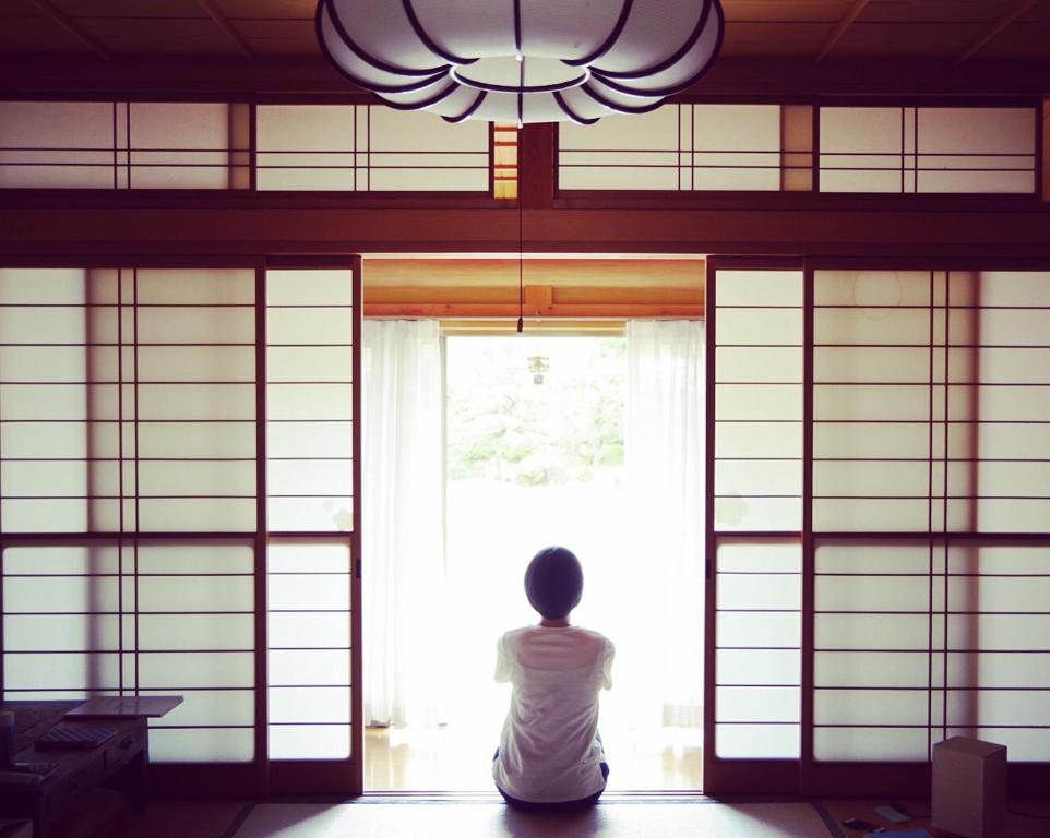 una persona seduta in una stanza che guarda fuori da una finestra di Guest House Warabi a Mino