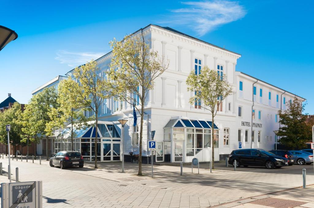 a white building on a street with cars parked in front at Hotel Phønix Hjørring in Hjørring