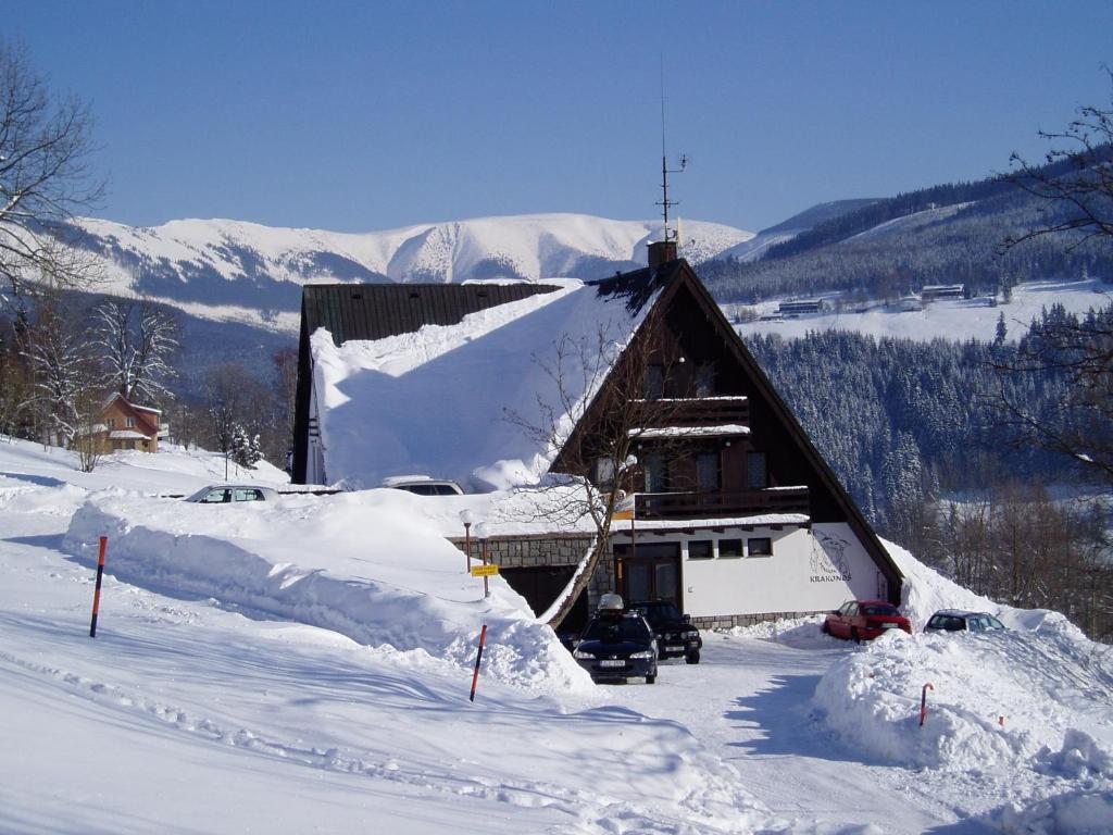 una casa ricoperta di neve con auto parcheggiate di fronte di Pension Krakonoš a Špindlerův Mlýn