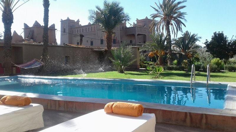 a swimming pool with two beds in front of a house at Dar Es Salam in Skoura