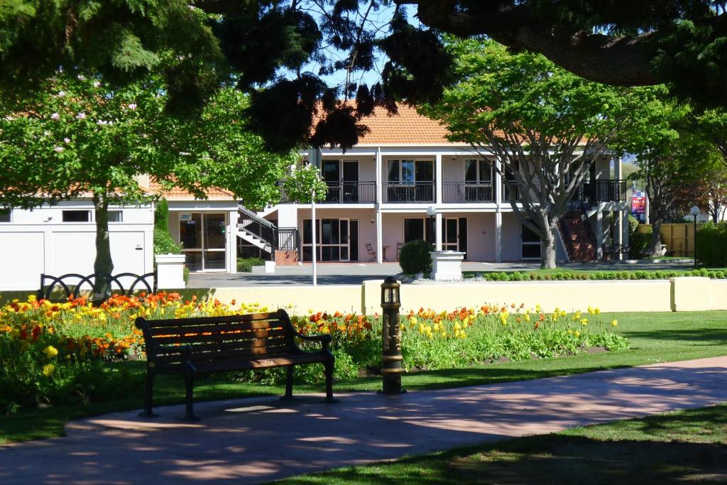 un banco de parque frente a un edificio con flores en Lugano Motor Lodge, en Blenheim