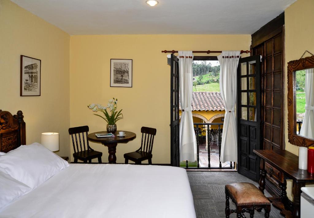 a bedroom with a bed and a table and a window at Hotel Hacienda El Salitre in Paipa