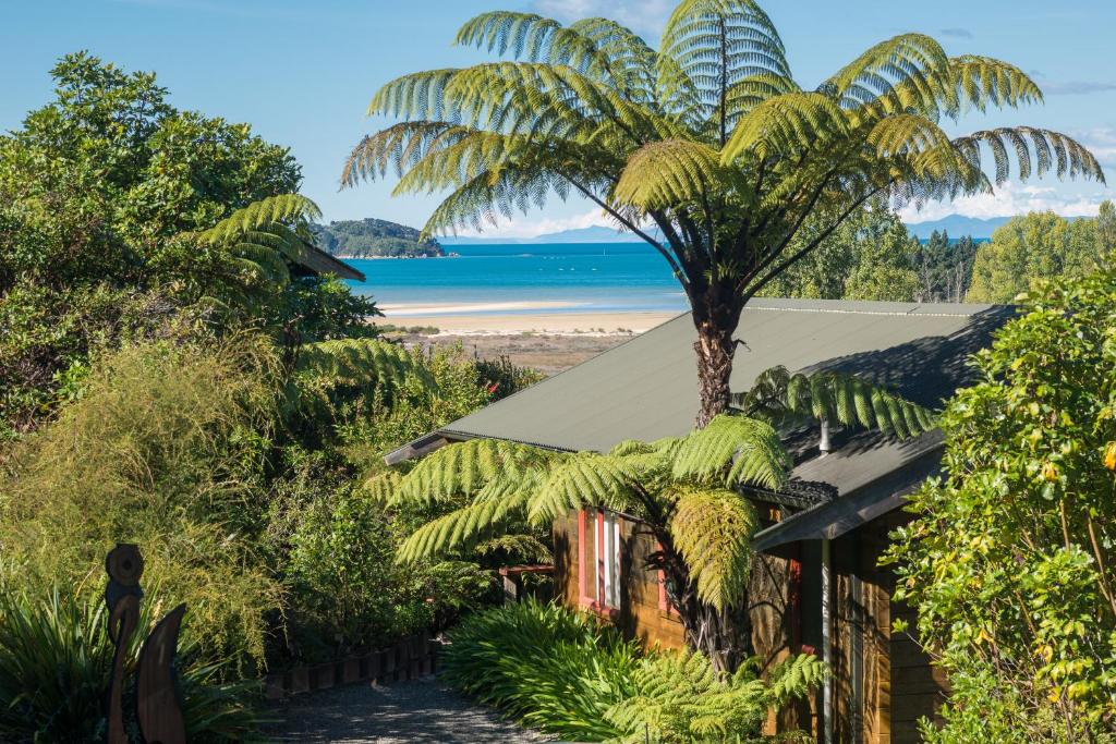 a palm tree in front of a house with a beach at Ocean View Chalets in Marahau