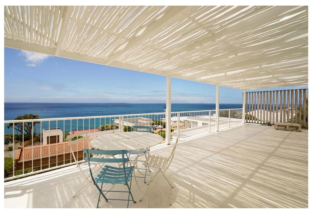 a balcony with a table and chairs and the ocean at Stunning Simonstown Apartment in Simonʼs Town