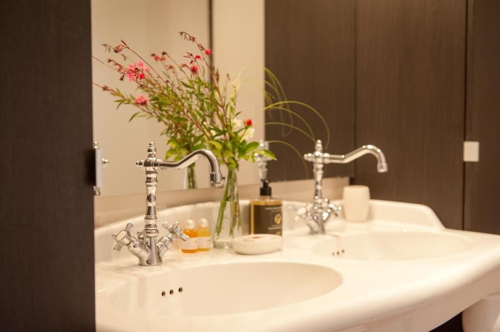 een wastafel in de badkamer met een vaas met bloemen erop bij Le Petit Matin in Bayeux
