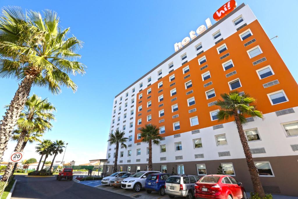 a hotel with palm trees and cars parked in a parking lot at Hotel Hi! Zapopan in Guadalajara