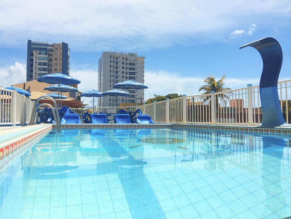 uma grande piscina com cadeiras azuis e guarda-sóis em Pousada Raio de Sol em Aracaju