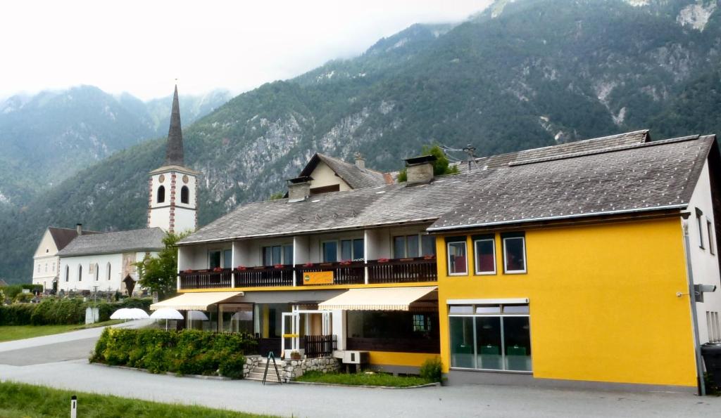 a yellow building with a church and a mountain at Gailtal Inn in Förolach