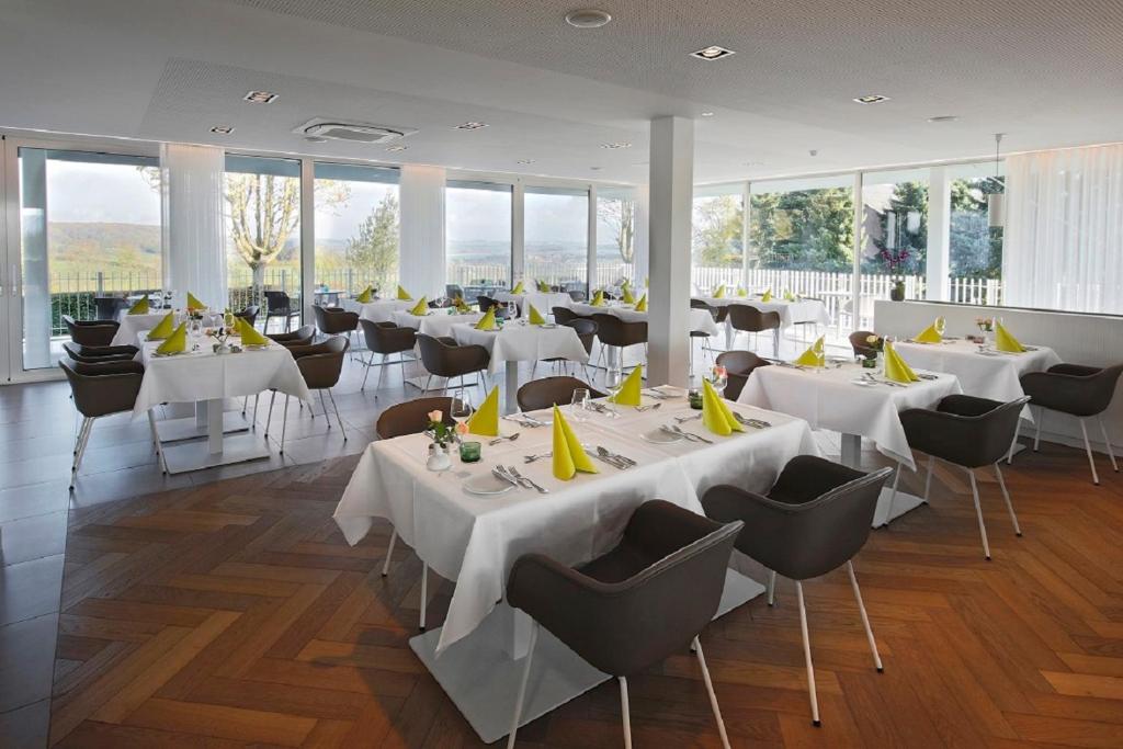 ein Restaurant mit weißen Tischen, Stühlen und Fenstern in der Unterkunft Hotel Berghoeve in Epen