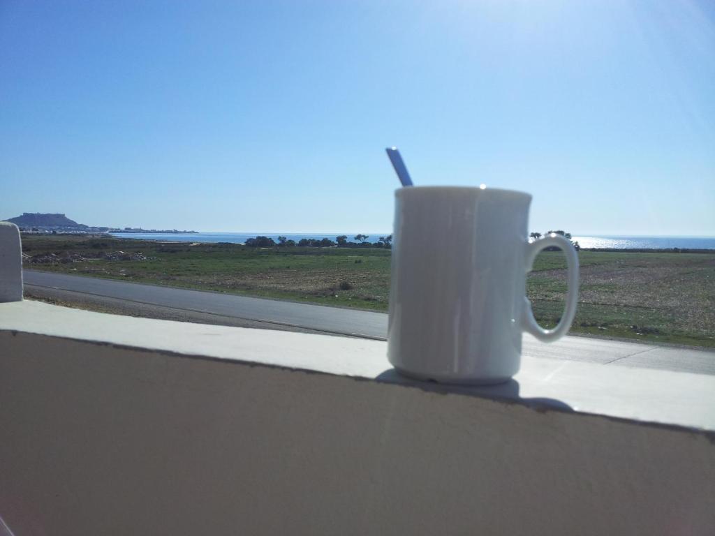 Una taza de café blanca sentada en el alféizar de la ventana en Luxus Apartments en Qulaybīyah