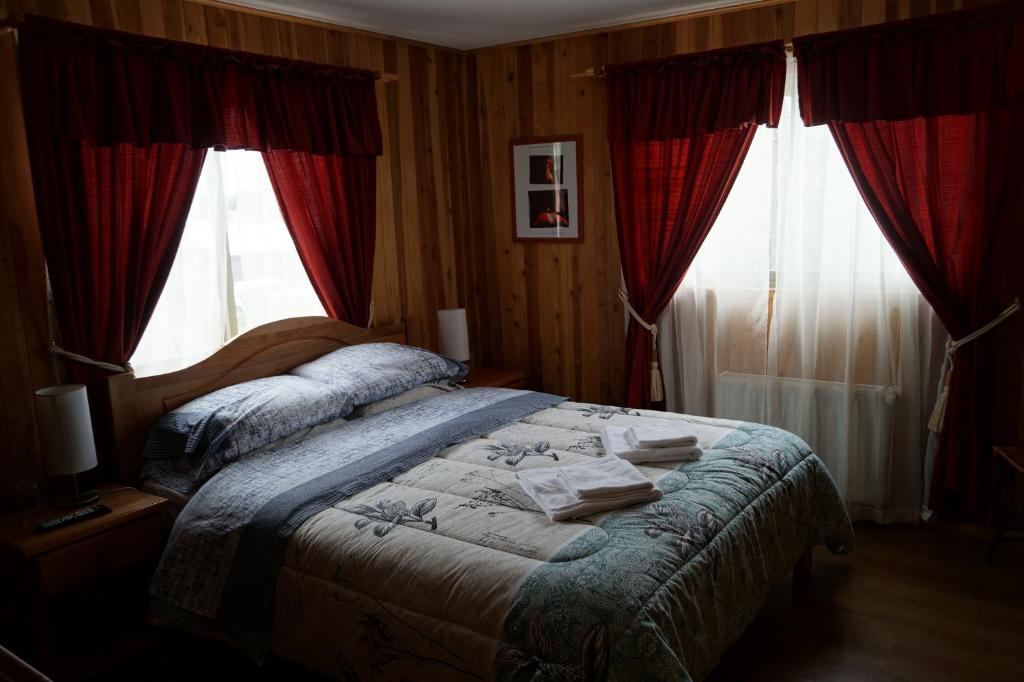 a bedroom with a bed and two windows with red curtains at Hostal Eifelhaus in Pucón