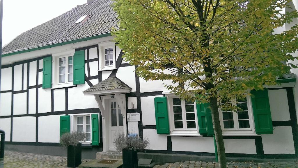 ein weißes und grünes Haus mit einem Baum davor in der Unterkunft Altes Pastorat in Solingen