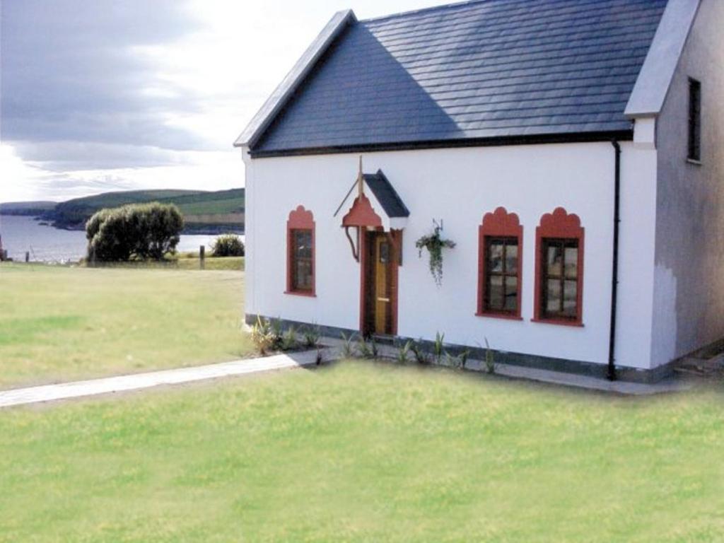una pequeña casa blanca con ventanas rojas en un campo de césped en Kinsale Coastal Cottages, en Garrylucas