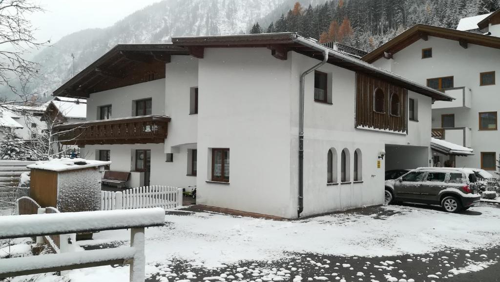 een besneeuwd huis met een auto ervoor geparkeerd bij Haus Huter in Kaunertal