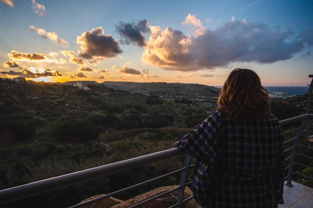 Eine Frau steht auf einem Balkon mit Blick auf den Sonnenuntergang. in der Unterkunft Paradise Gardens in Xagħra
