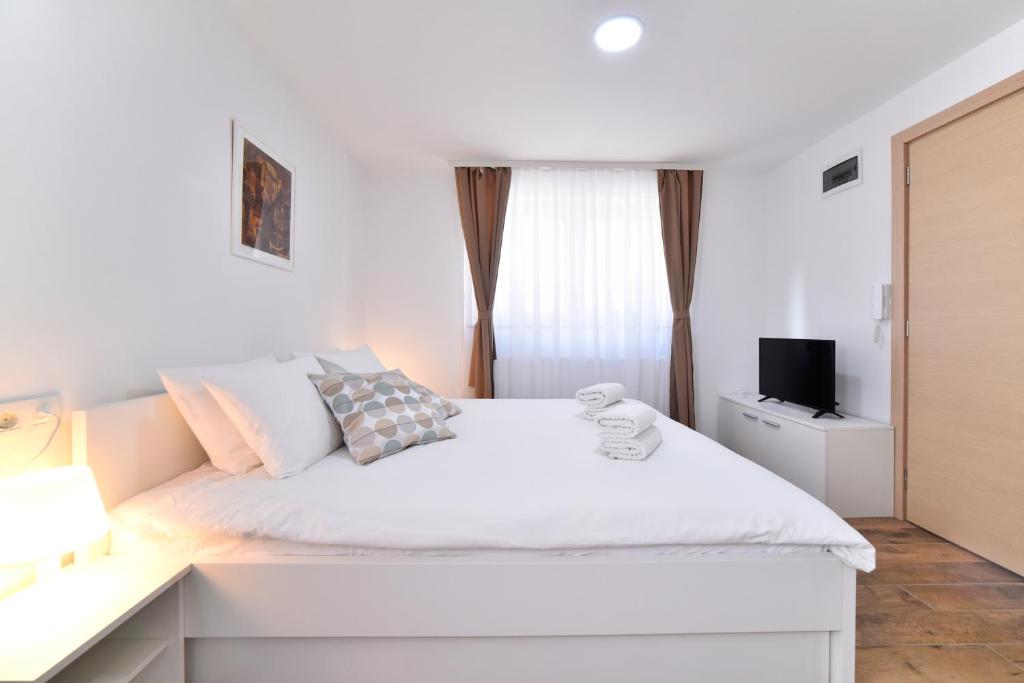 a white bedroom with a white bed and a television at Piccolo Apartments in Zagreb