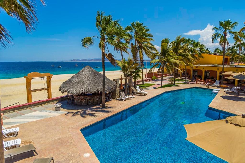 a swimming pool next to a beach with palm trees at Hotel Playa Del Sol in Los Barriles