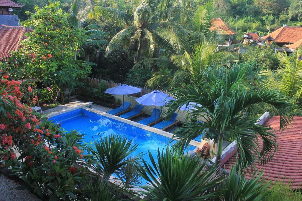 a pool in a garden with palm trees and blue umbrellas at Breeze Villa in Nusa Lembongan