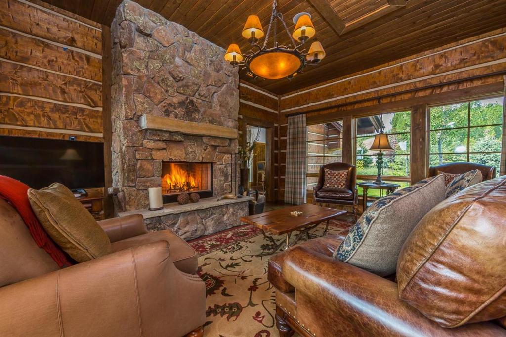 a living room with leather furniture and a stone fireplace at Spanish Peaks Settlement Cabin in Big Sky