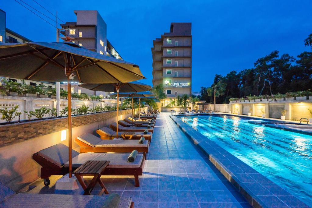 a swimming pool with lounge chairs and umbrellas at night at Olive Tree Hotel in Na Jomtien