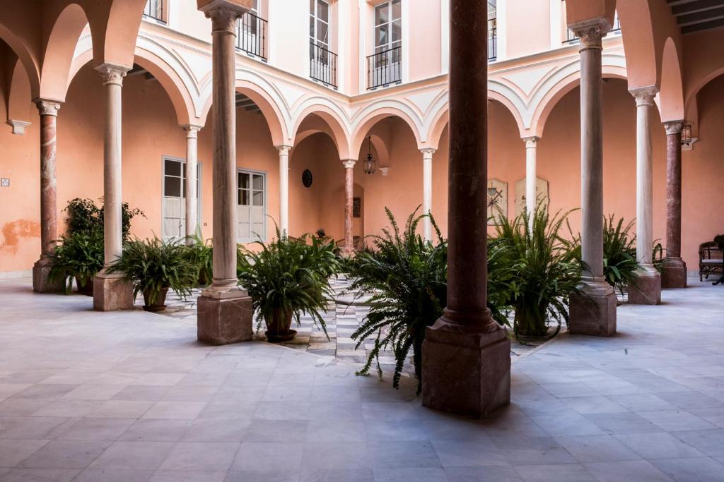 un bâtiment avec des colonnes et des plantes en pot dans une cour dans l'établissement Palacio Mármoles, à Séville