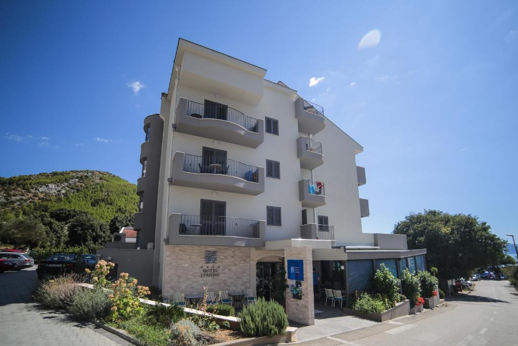 ein hohes weißes Gebäude mit Balkonen auf einer Straße in der Unterkunft Hotel Ivando in Drvenik