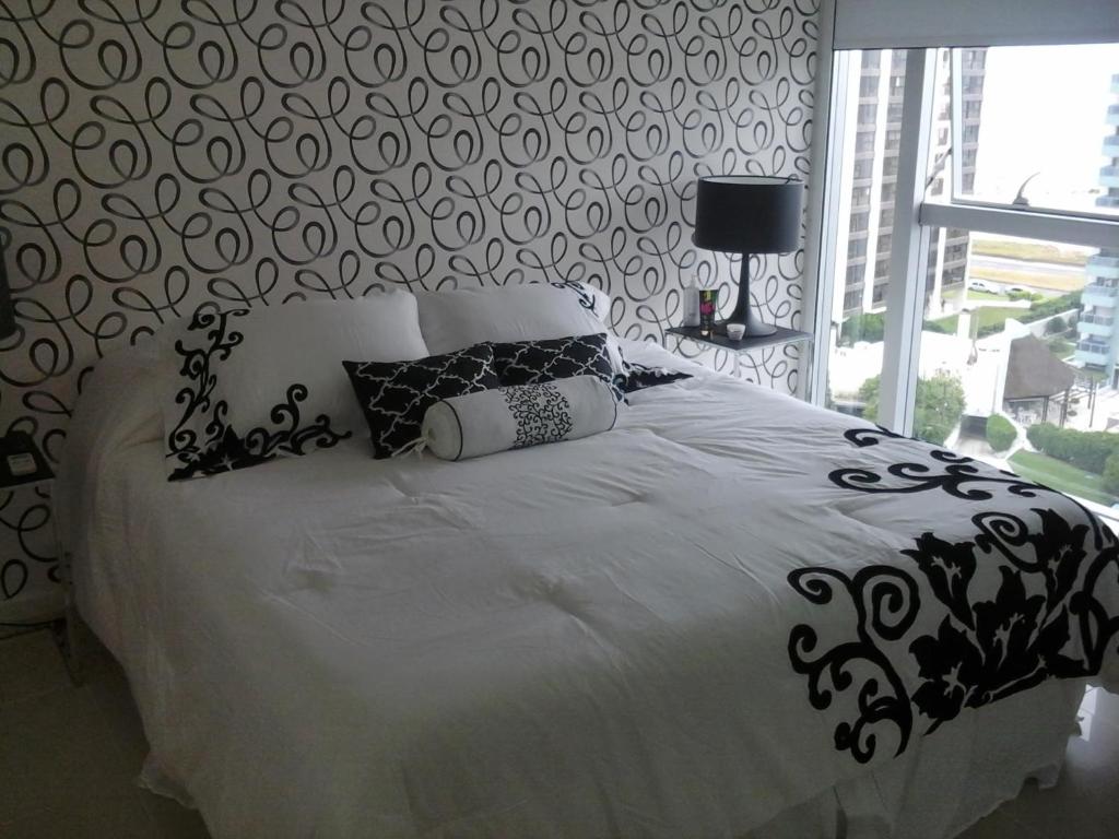 ein Bett mit schwarzen und weißen Kissen und einem Fenster in der Unterkunft Apartamento en Punta del Este in Punta del Este