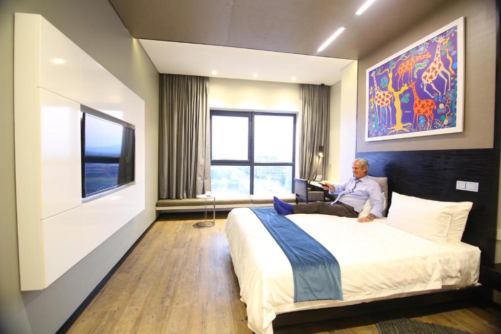 Room50Two في غابورون: رجل يجلس على سرير في غرفة فندق