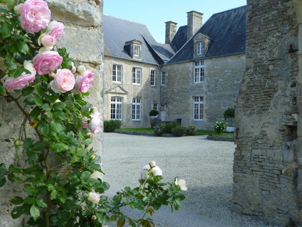 un edificio de piedra con rosas rosas delante de él en Manoir de L'Hermerel, en Géfosse-Fontenay