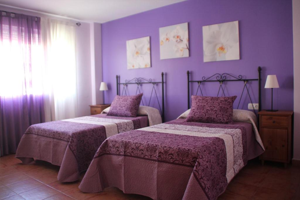 2 camas en una habitación con paredes moradas en Hostal Zaguan en Talaveruela