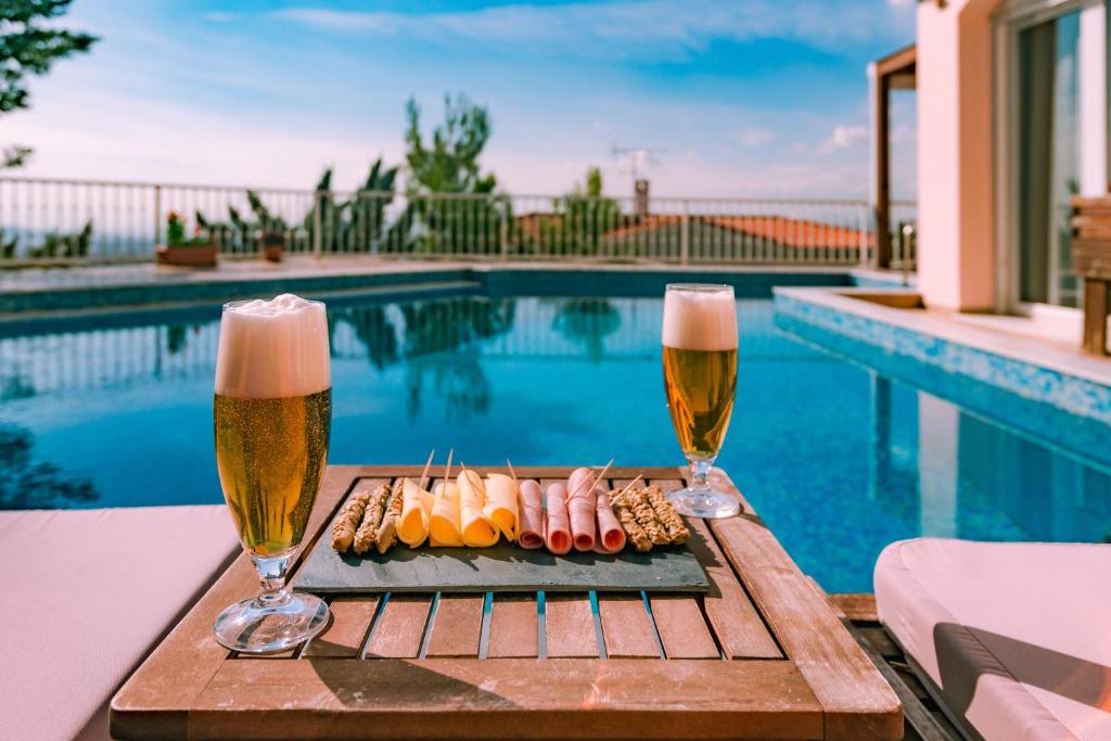 zwei Gläser Bier und ein Tablett mit Essen neben einem Pool in der Unterkunft Villa Politia in Athen