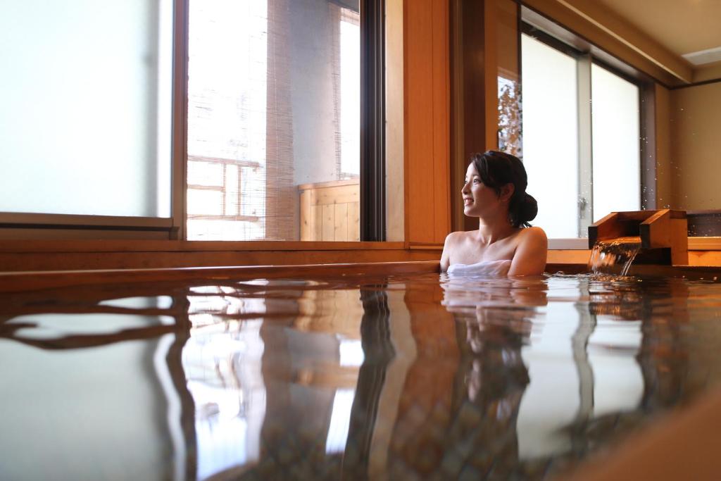 une femme est assise dans une piscine dans l'établissement こんぴら温泉 貸切湯の宿 ことね, à Kotohira