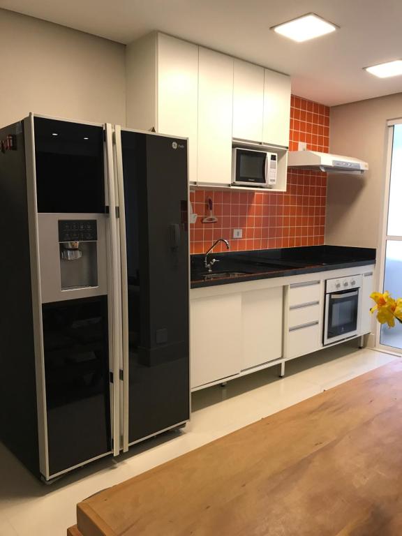 uma cozinha com electrodomésticos pretos e armários brancos em Apartamento Zapata Guarujá no Guarujá