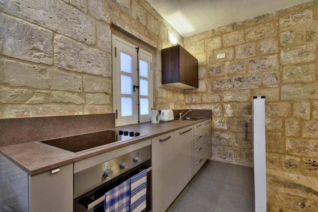 cocina con paredes de piedra, fregadero y fogones en Vallettastay Standard Apartments in Valletta, en La Valeta
