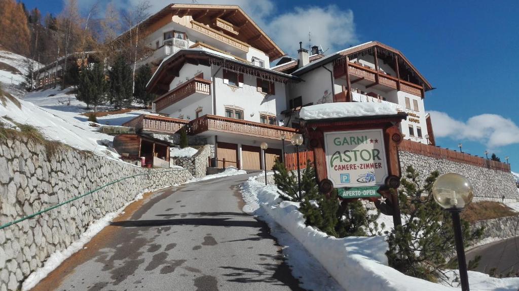 a building on a snow covered road with a sign in front at Garnì Astor in Arabba