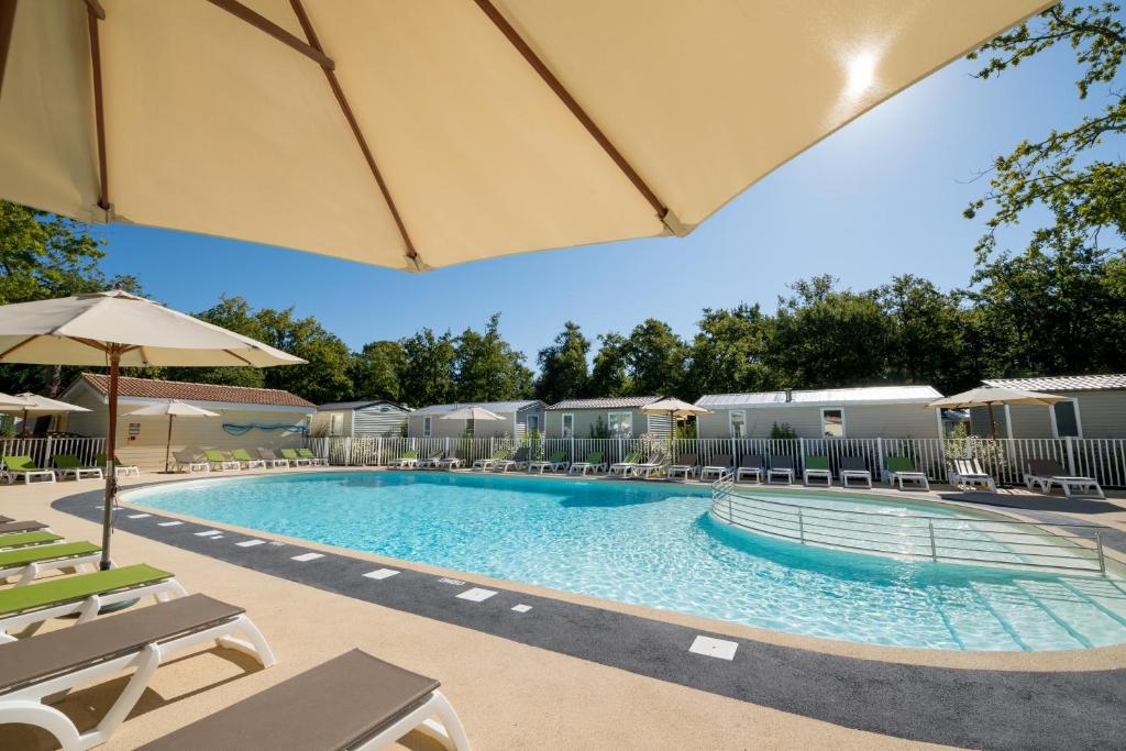 a pool at a resort with chairs and an umbrella at Camping Les Chèvrefeuilles in Royan