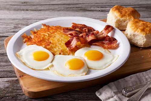 a plate of eggs and bacon on a wooden table at AS Apartments in Kopaonik
