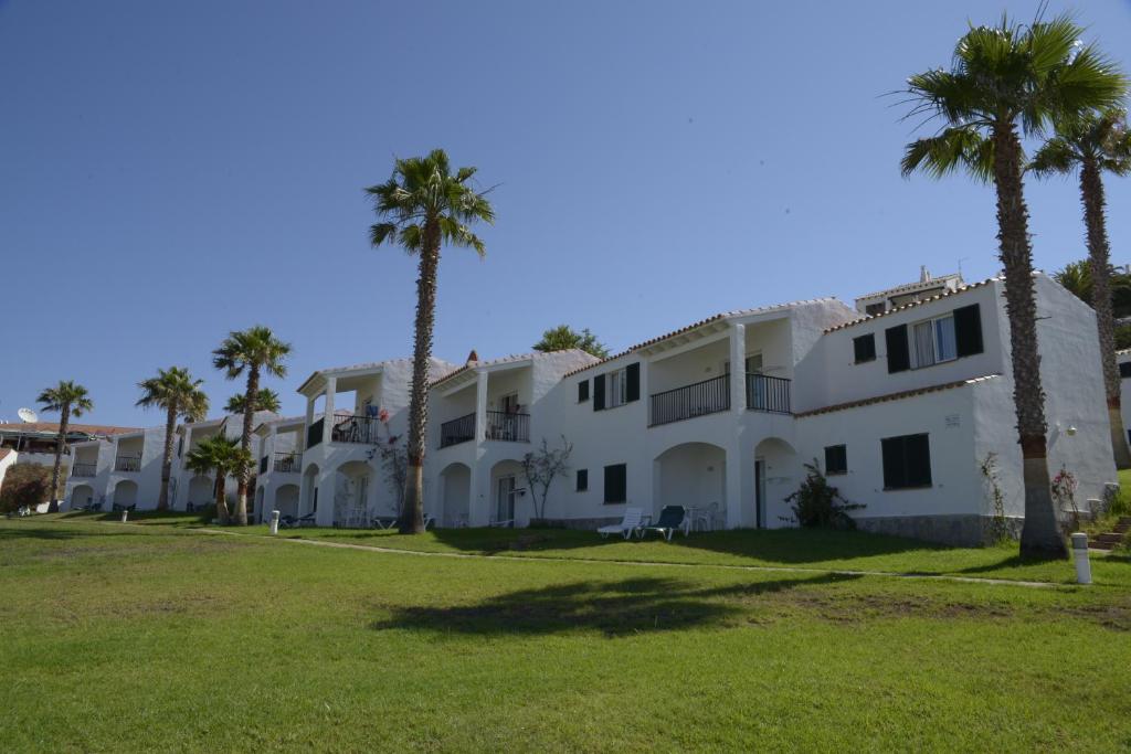 Un gran edificio blanco con palmeras delante. en TRH Tirant Playa, en Fornells