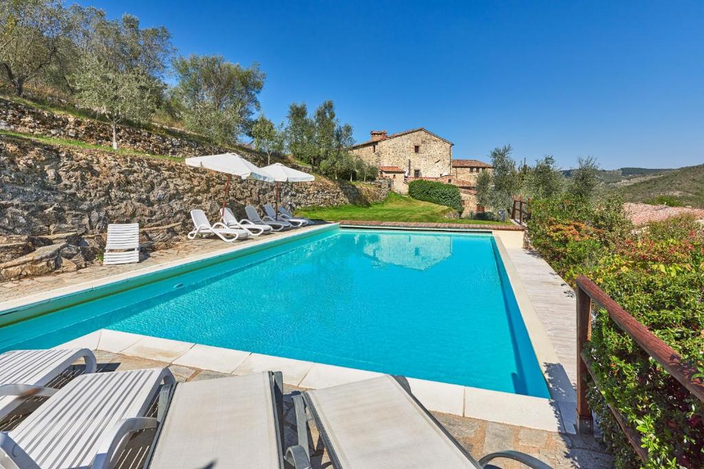 a swimming pool with chairs and a house at Casale il Gualdo by VacaVilla in Radda in Chianti