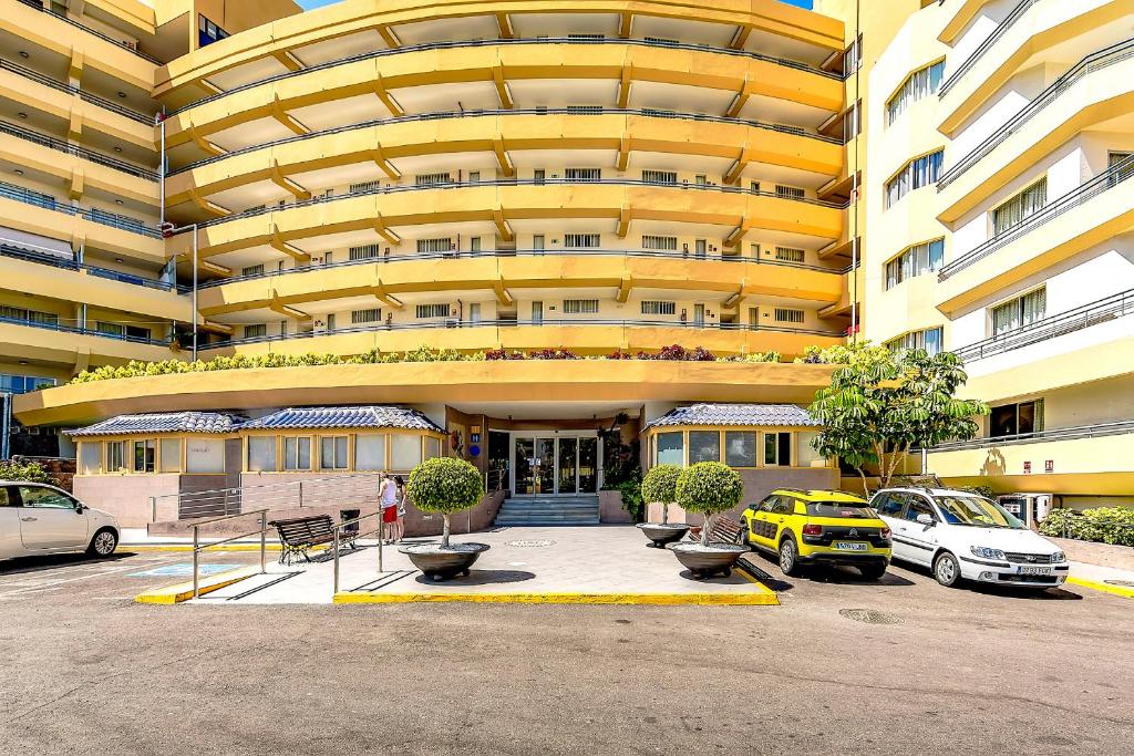 a large yellow building with cars parked in a parking lot at Santa Maria 2 bedrooms in Adeje