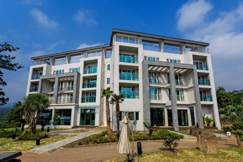 a large white building with palm trees in front of it at Jeju M Resort in Seogwipo