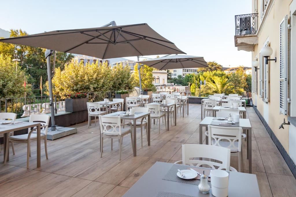 ロカルノにあるオテル デュ ラックのテーブルと椅子、傘が備わるレストラン