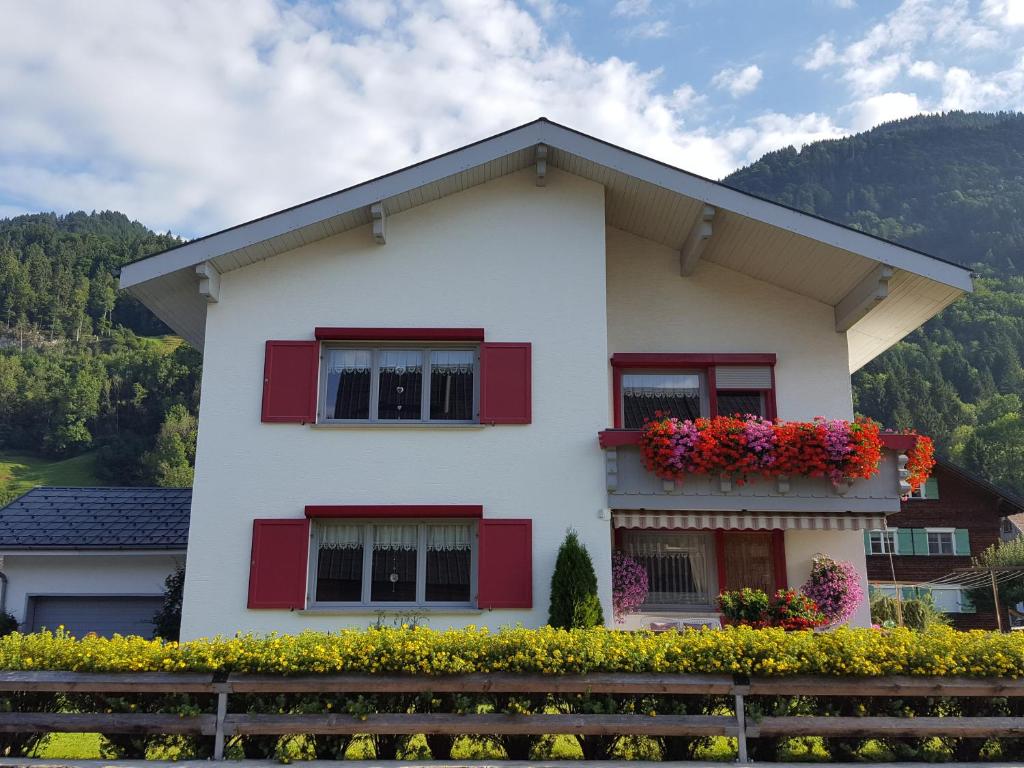 ein weißes Haus mit roten Fensterläden und Blumen in der Unterkunft Appartements Gästehaus Monika in Bezau