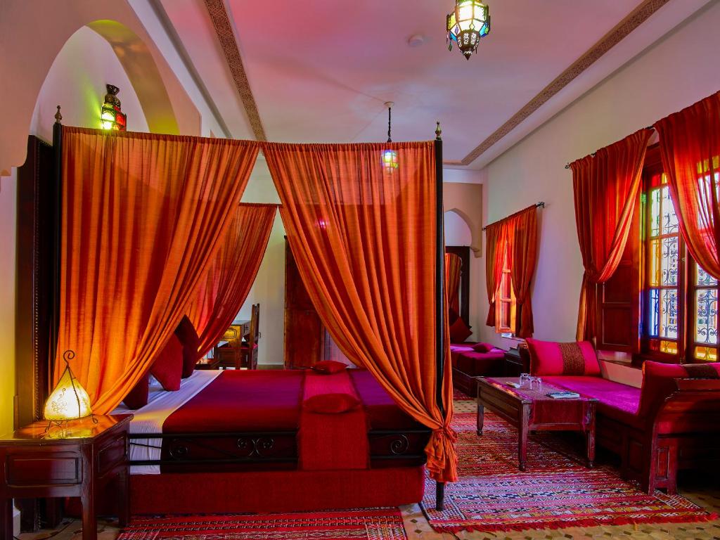 een slaapkamer met een bed met rode gordijnen en een bank bij Riad Ahlam in Fès