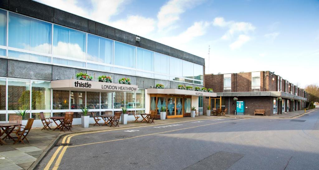 a building with tables and chairs in front of a street at Thistle London Heathrow Terminal 5 in Hillingdon
